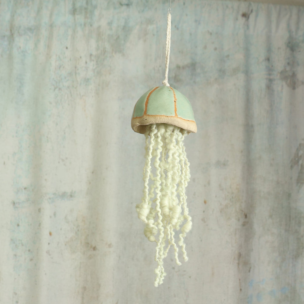 Mint green ceramic jellyfish with wool tentacles hangs in from of a moody background