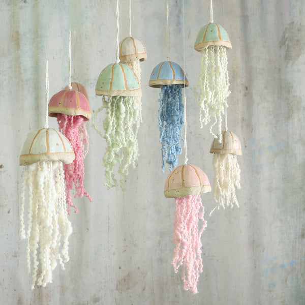 a shoal of colourful ceramic jellyfish with hand dyed wool tentacals hang at different heights in from of a soft grey backgound - Handmade Ceramic Jellyfish hangings by Habulous Ceramics 
