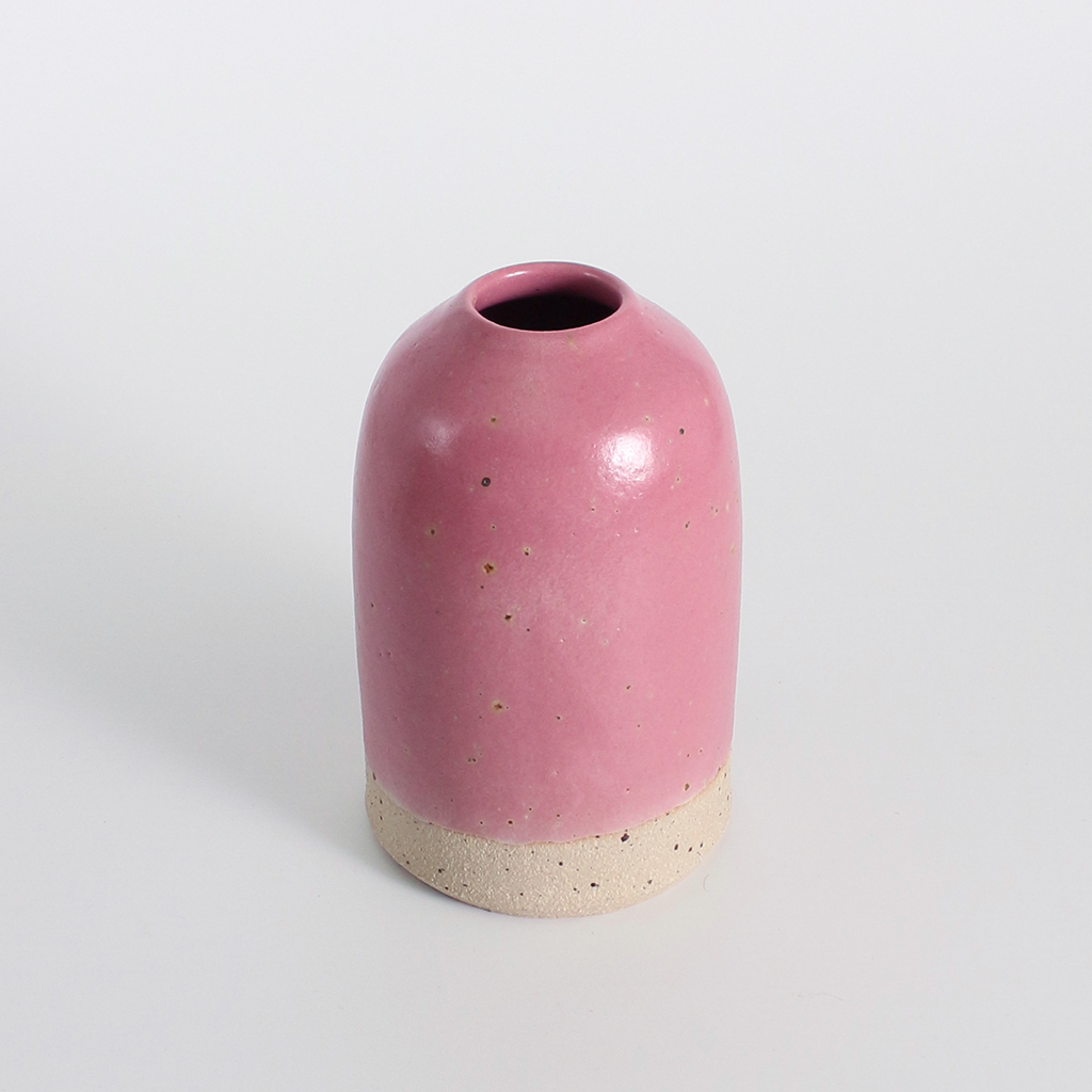 Pink ceramic bud vase with a beige base on a light grey background
