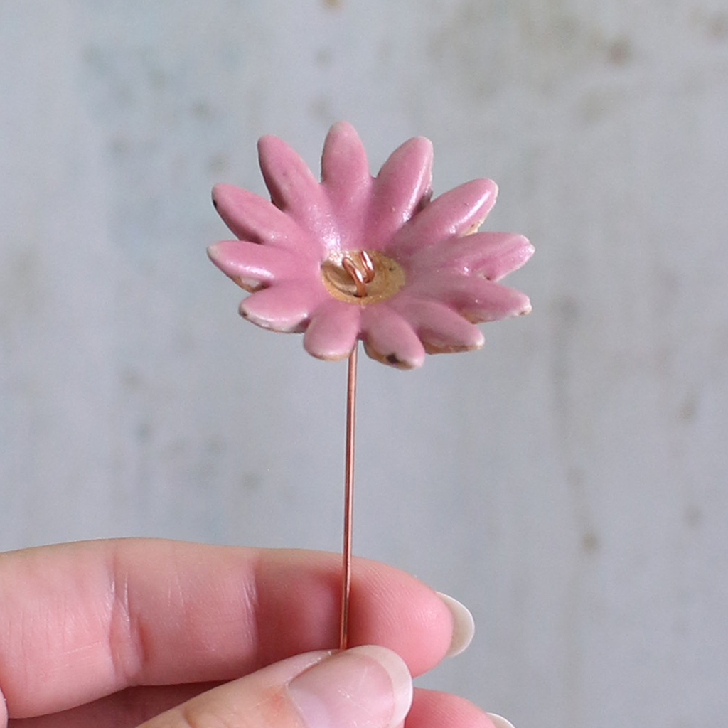 Fuchsia ceramic flower held by a hand against a neutral background