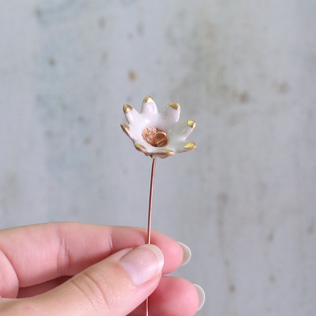 Small white flower with gold accents held by a hand against a neutral background