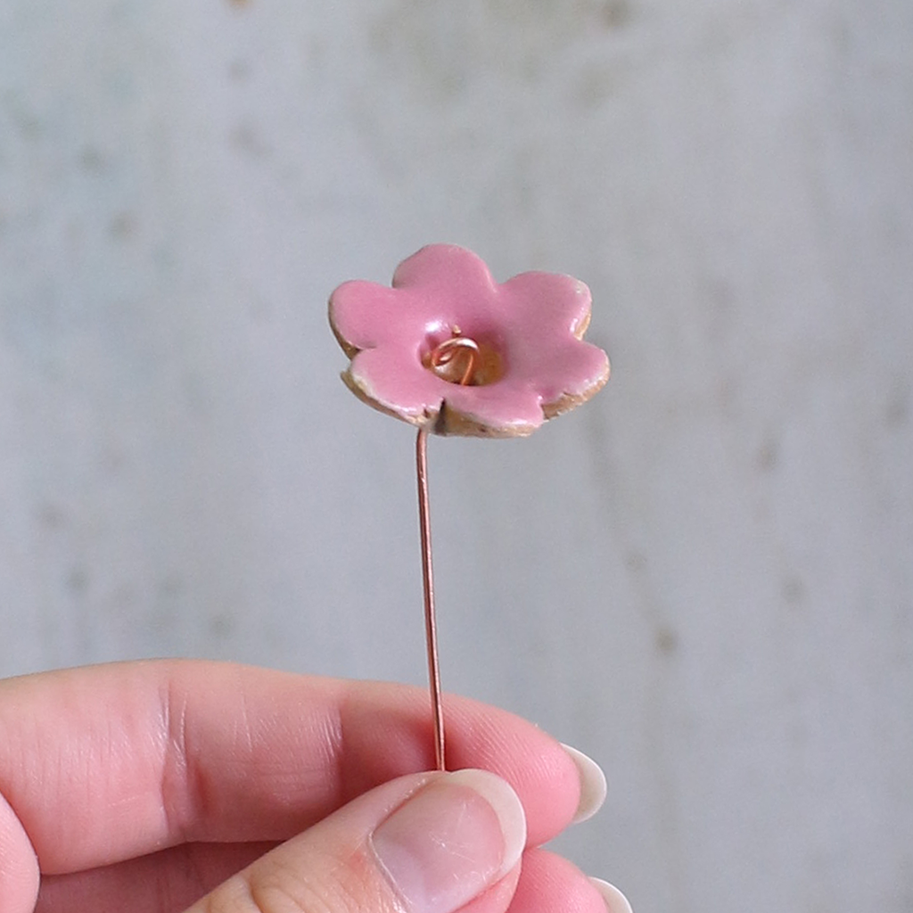 Pink ceramic flower held between fingers against a neutral background