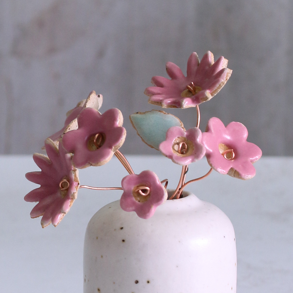 Small ceramic vase with pink flowers on a neutral background