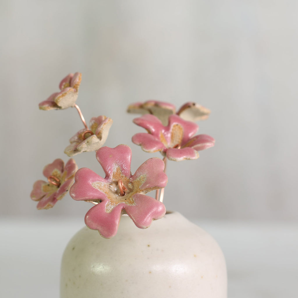 Bright pink ceramic flowers on copper wire in a small handmade white vase 