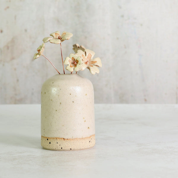 Speckled beige ceramic vase with handmade ceramic primrose flowers in a light yellow on a light background