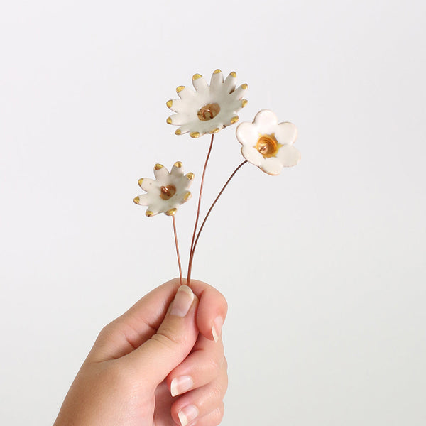 Hand holding three white flowers with gold centers against a light gray background