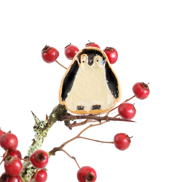 Penguin-shaped plant hugger on a branch with red berries