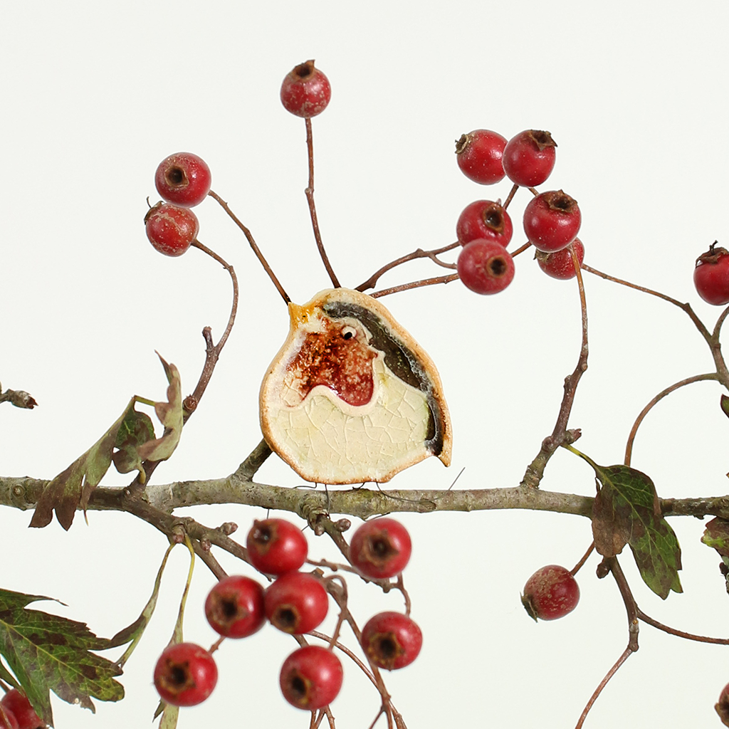Ceramic robin on a branch with red berries.
