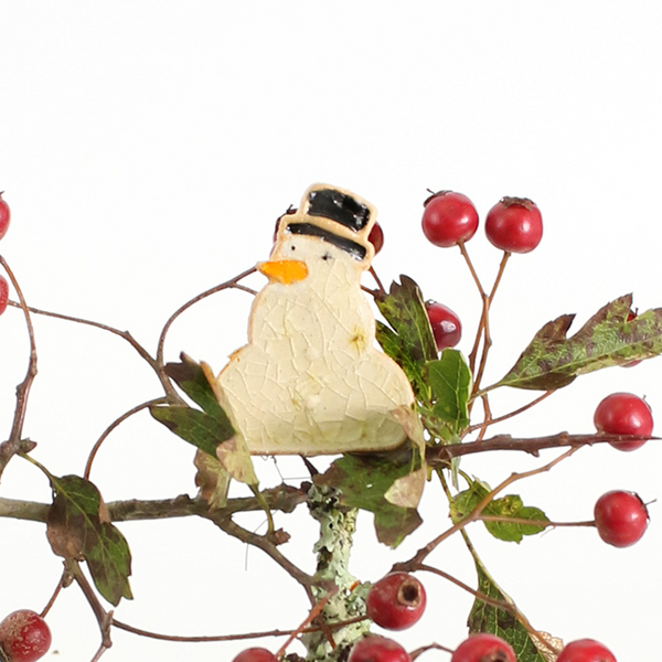 Decorative snowman ornament on a branch with red berries