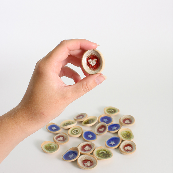 Hand holding a small ceramic worry stone with a blue star design, surrounded by other similar discs on a white background.