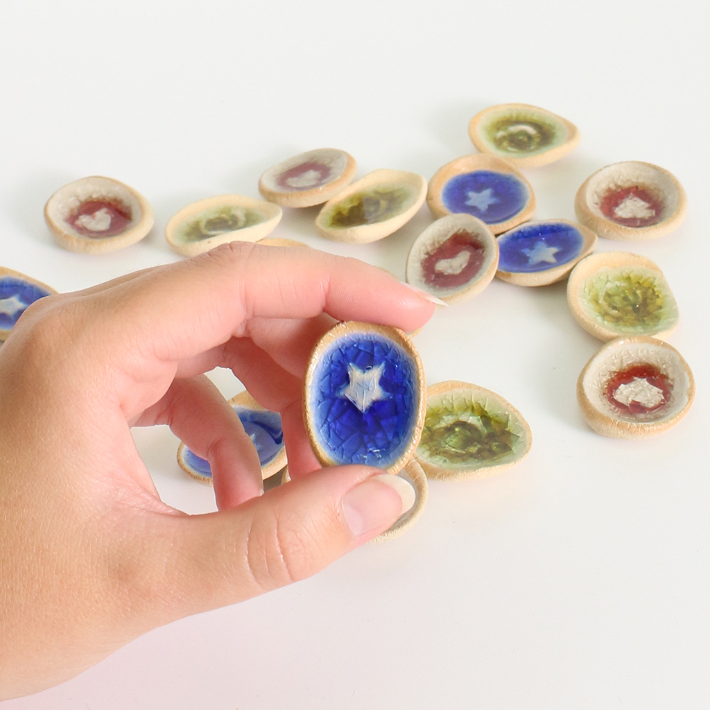 Hand holding a small ceramic worry stone with a blue star design, surrounded by other similar discs on a white background.