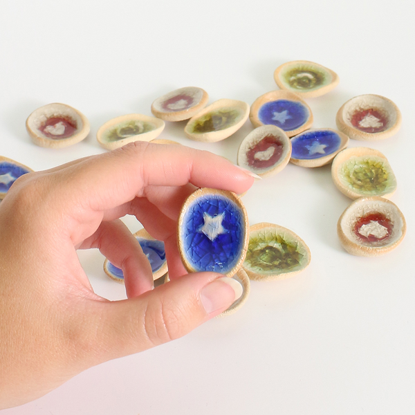 Hand holding a small ceramic worry stone with a blue star design, surrounded by other similar discs on a white background.