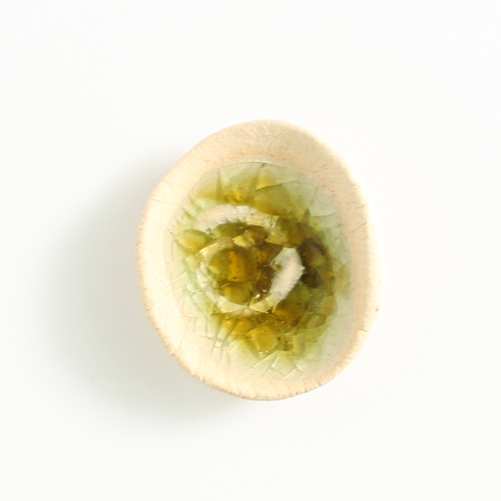 Round ceramic worry pebble with a green stone in the centre on a white background