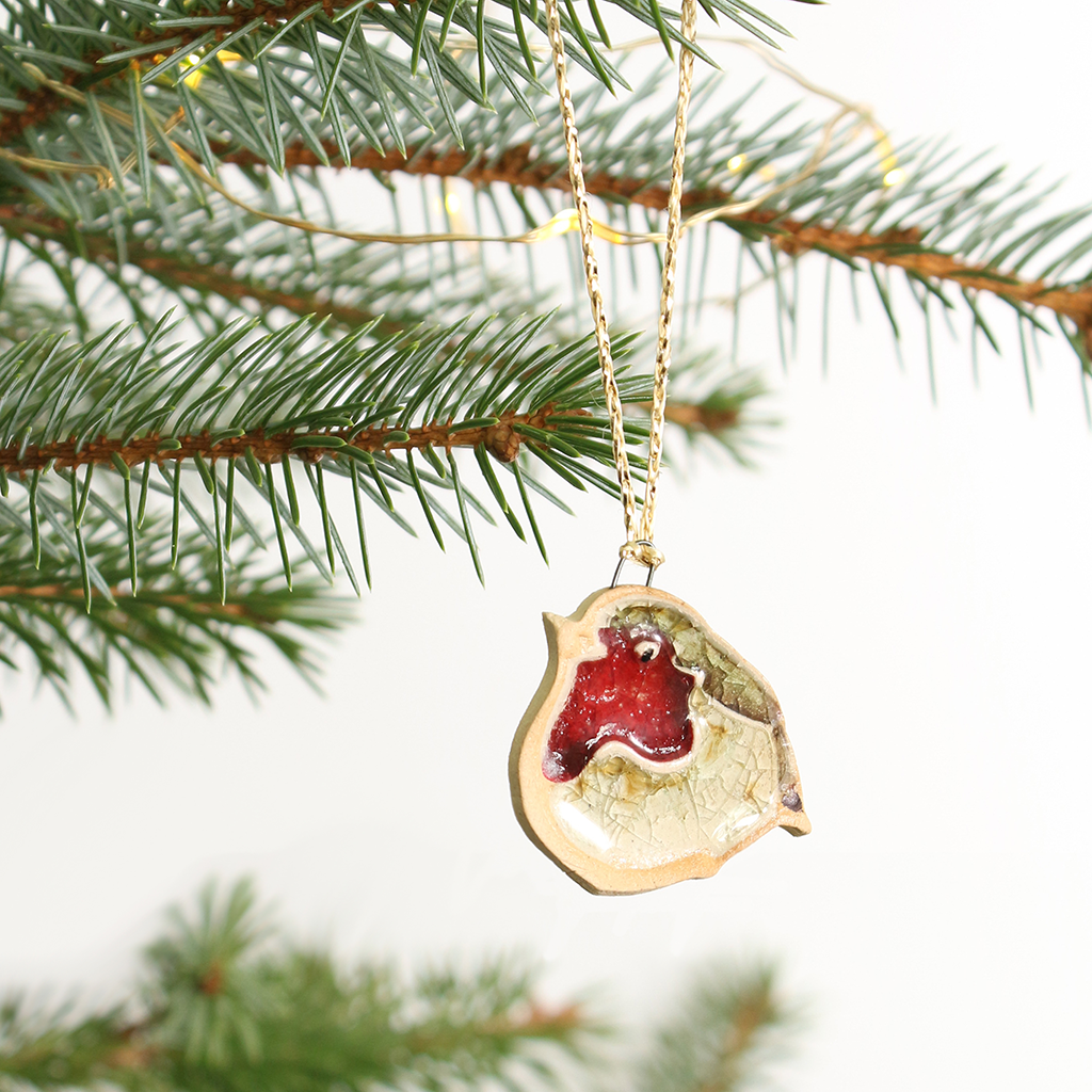 Decorative robin ornament hanging on a gold chain against a green Christmas tree background.