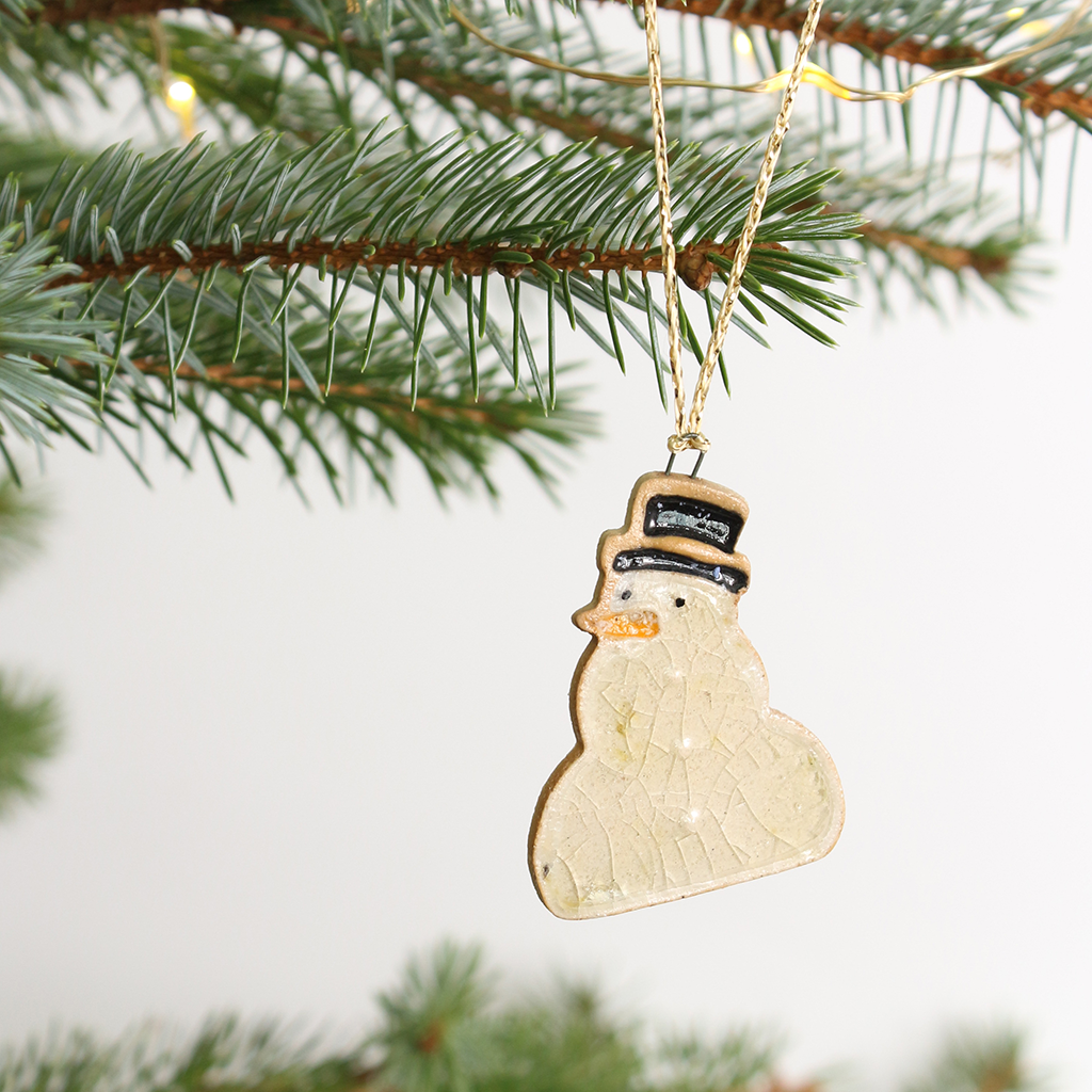 Ceramic snowman ornament hanging on a Christmas tree branch.