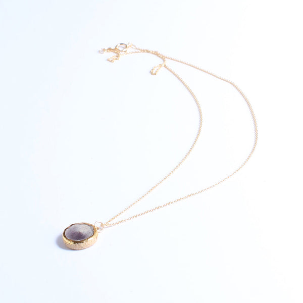 Gold necklace with a purple pendant on a white background