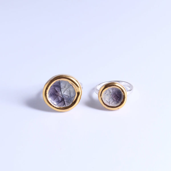 Large and small silver rings with ceramic and glass charms. Each ring features smoky-purple coloured glass and gold lustre detailing around the edge. The rings are placed side-by-side to show their size comparision. 